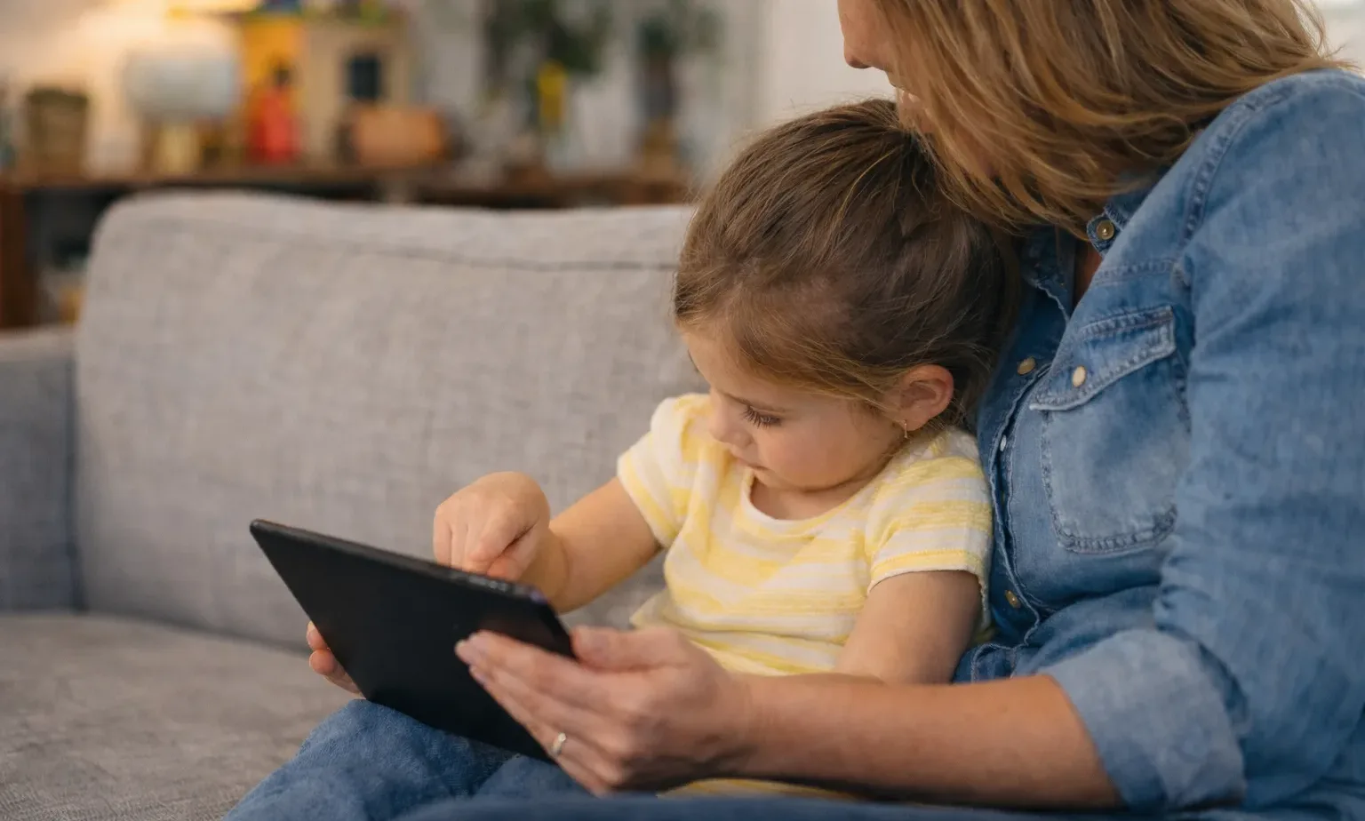 Woman and young girl using a tablet together on a couch