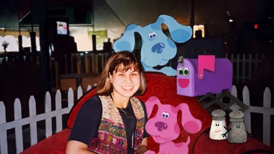 Allison Caplovitz. PhD sits in a red chair on the set of kids TV show Blue's Clues alongside several characters from show. Photo taken in 1998.
